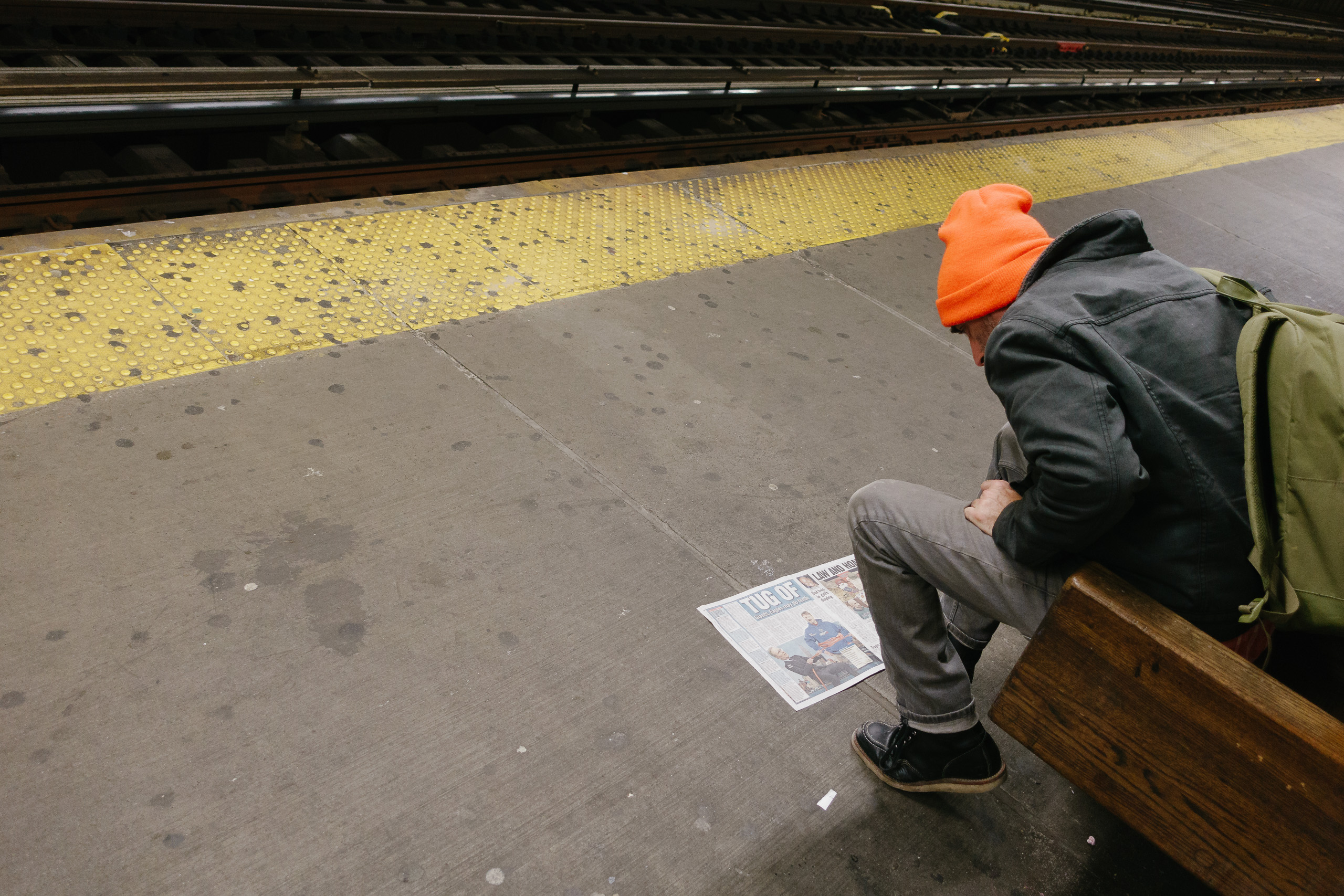 Man reading NY Daily News or something on the subway platform