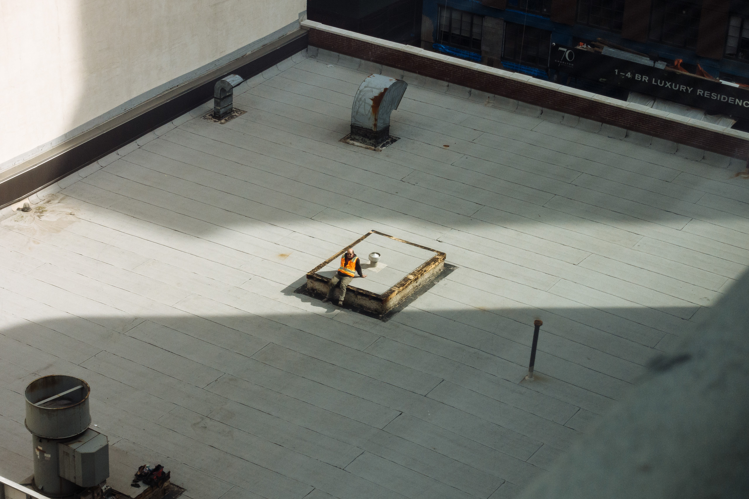 A worker rests on a rooftop in the sun passing between two highrises