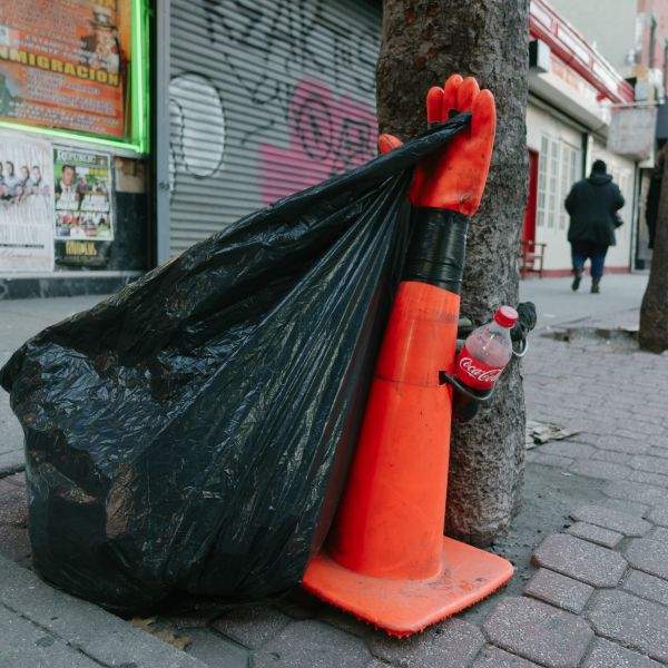 Garbage bag attached to a small, gloved traffic cone.