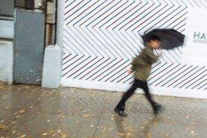 A man under an umbrella dashes past a barber shop Houston Street