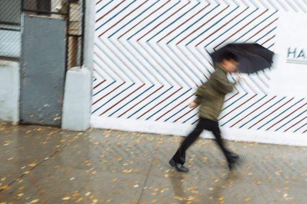 A man under an umbrella dashes past a barber shop Houston Street