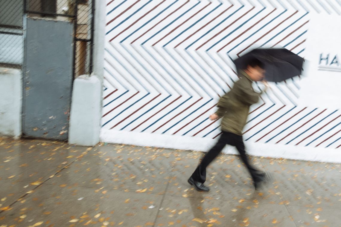 A man under an umbrella dashes past a barber shop Houston Street