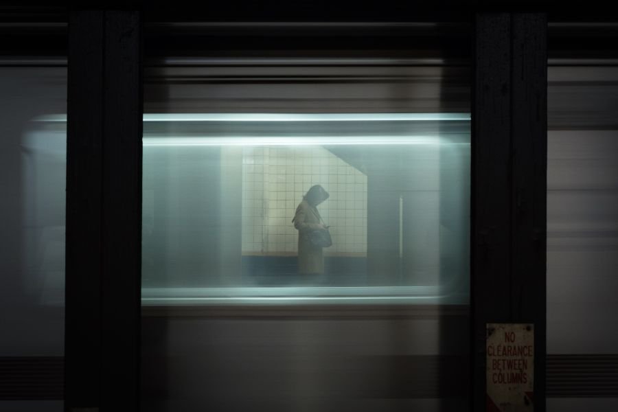 A passenger waits for the uptown 1 train, as seen through the passing 2 train
